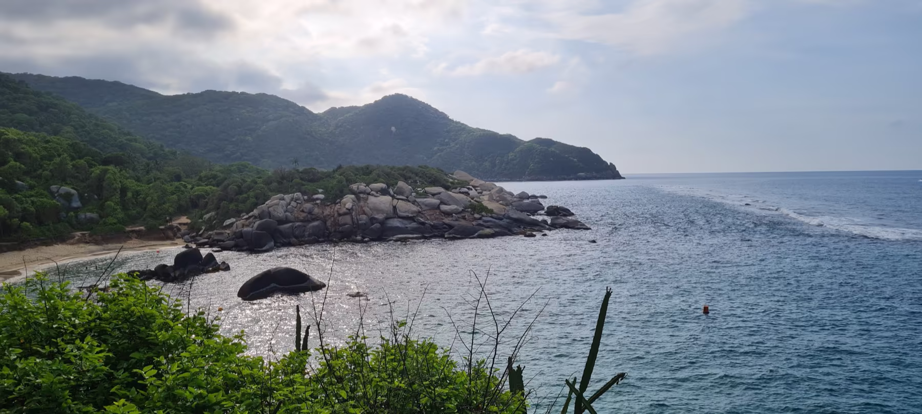 Vista panorámica de una bahía rocosa entre montañas boscosas y el mar Caribe abierto